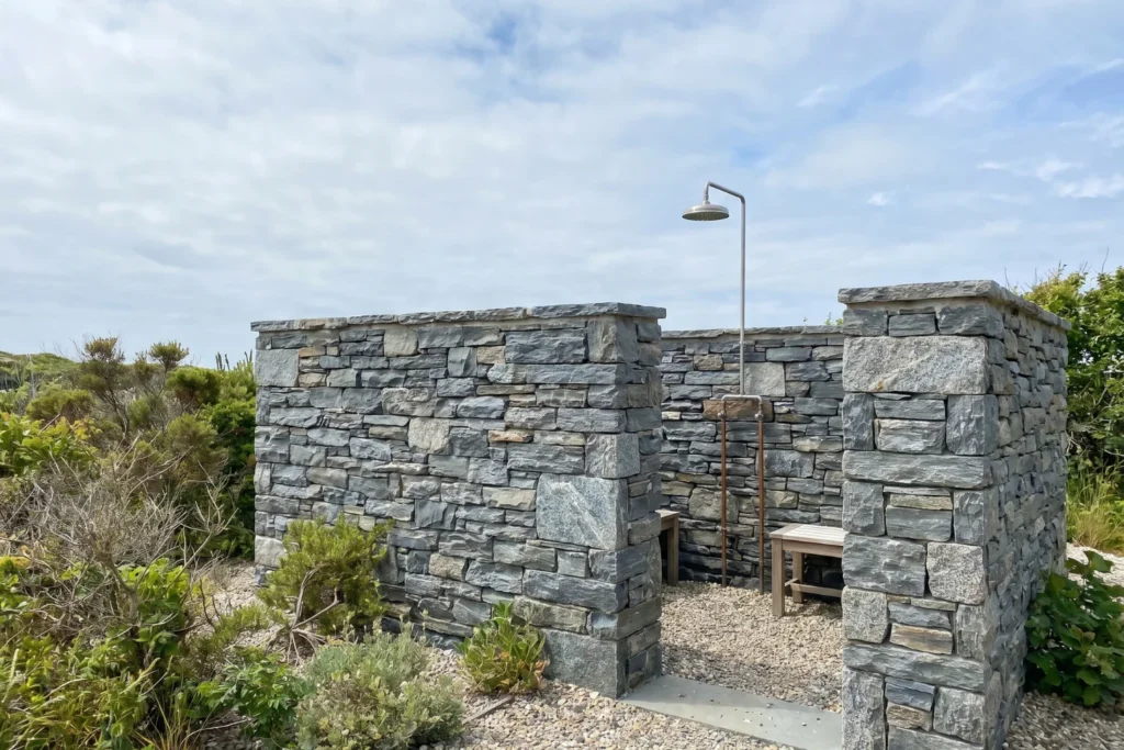 Stone half-wall outdoor shower enclosure for wind protection in outdoor bathroom privacy design