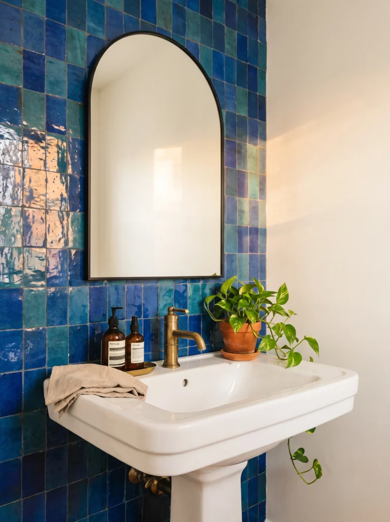 guest bathroom with glossy cobalt and teal zellige tile wall, black arched mirror, and white pedestal sink