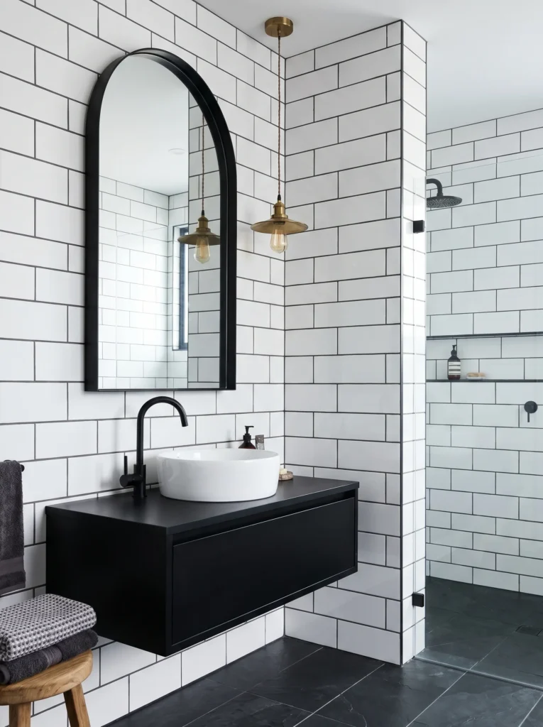 Bathroom with white subway tile in dark charcoal grout, large arched matte black mirror, floating black vanity, matte black faucet, and vintage brass pendant light