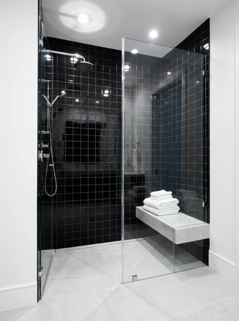 Glossy black square tile shower with chrome fixtures and a floating grey stone bench