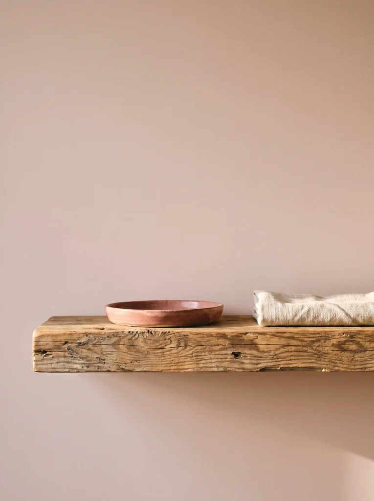Thick reclaimed wood shelf on a blush pink wall holding a pink stoneware dish and folded cream linen