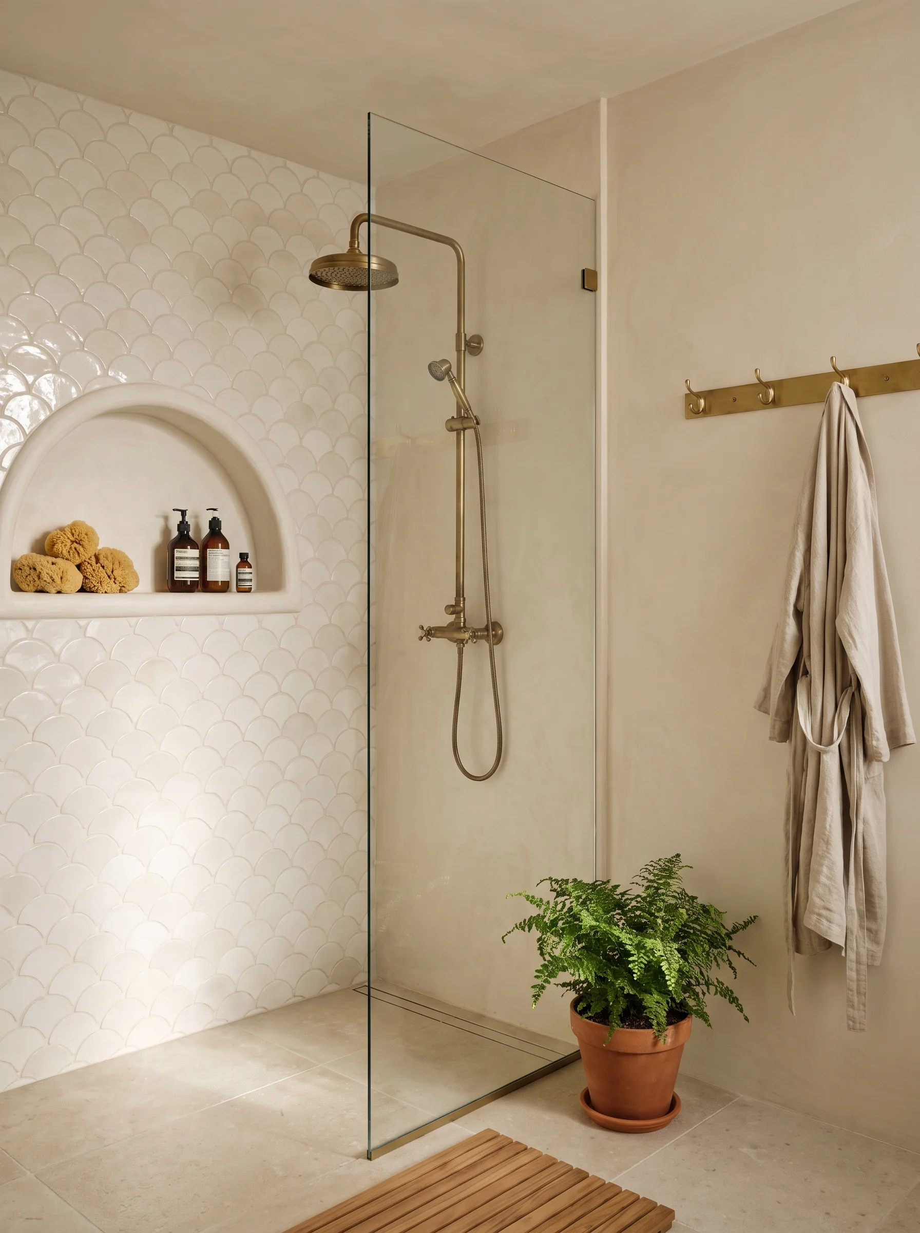 walk in shower with cream fish scale tile, arched niche, brass exposed shower, and teak bath mat
