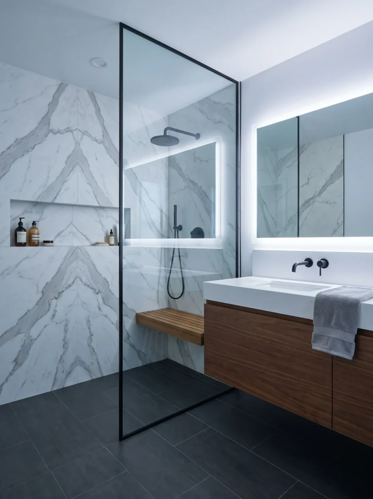 Modern master bathroom with book matched marble slab shower, black fixtures, teak fold down bench, walnut floating vanity, and charcoal floor tile