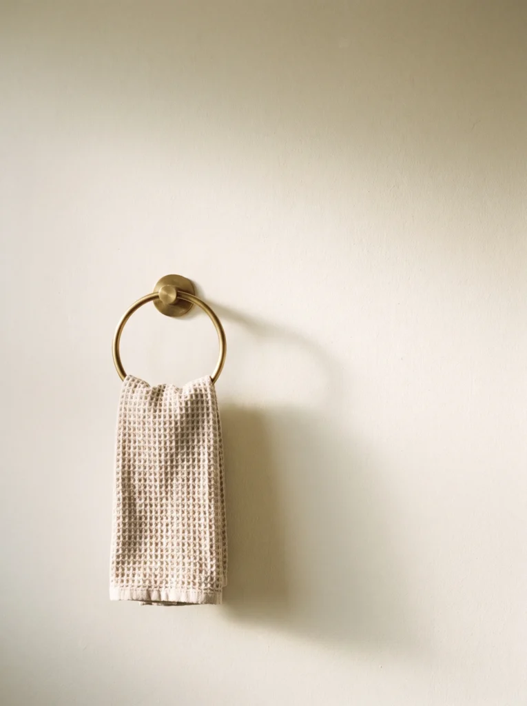A brushed brass towel ring on a cream plaster wall holding a folded waffle hand towel