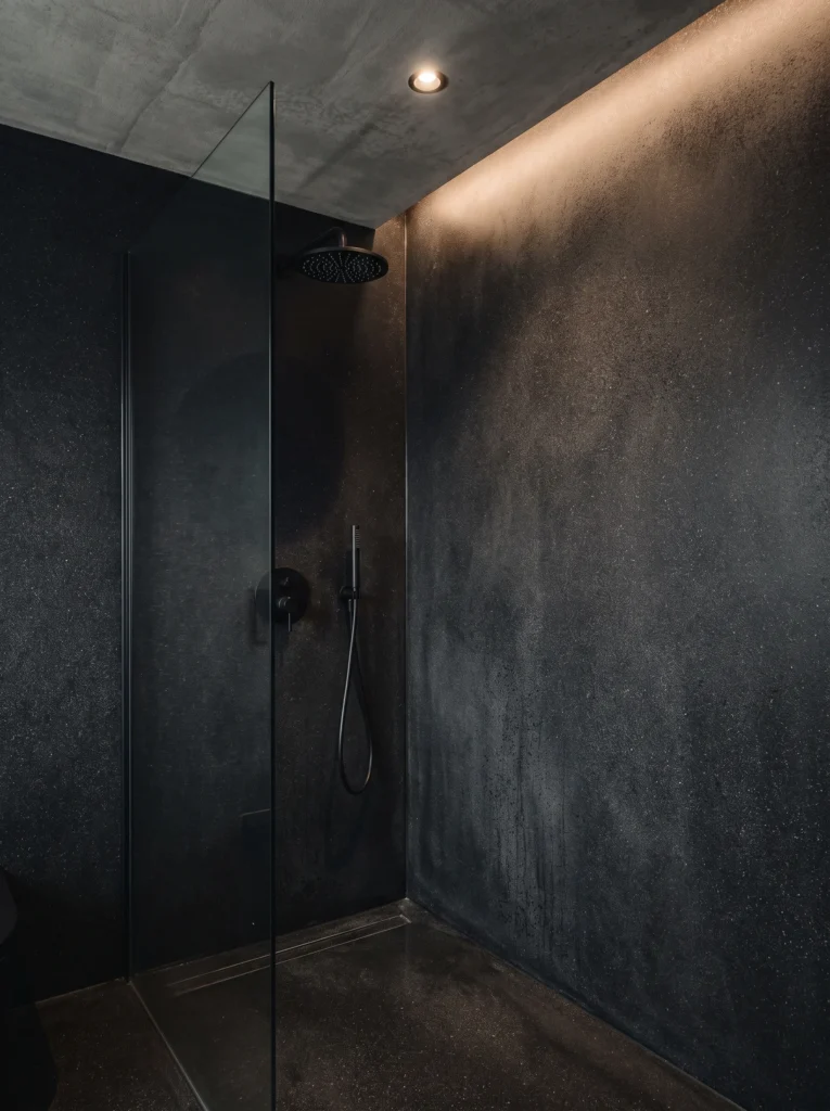dark speckled microcement shower with matte black fittings, glass panel and hidden cove ceiling lighting