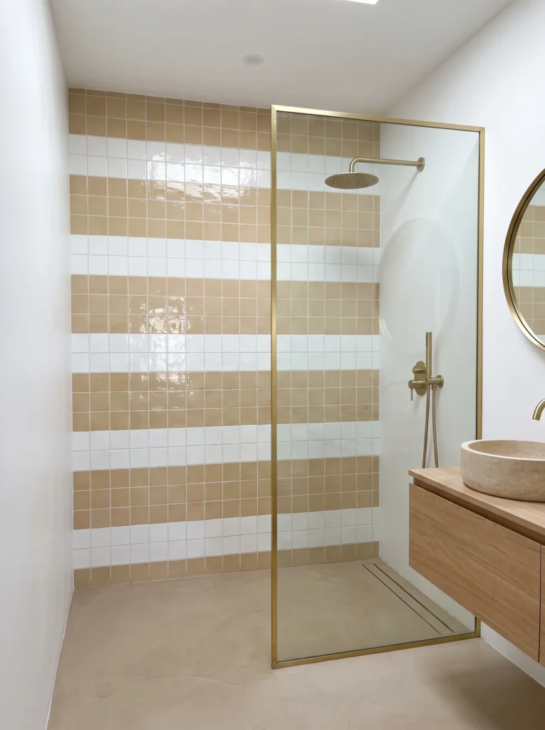 beige and white horizontal striped square tile shower wall with brass framed glass panel and travertine vessel sink