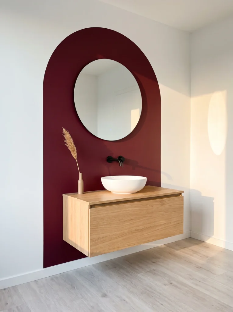 burgundy painted arch on white wall with round LED mirror, floating oak vanity, and white vessel bowl sink