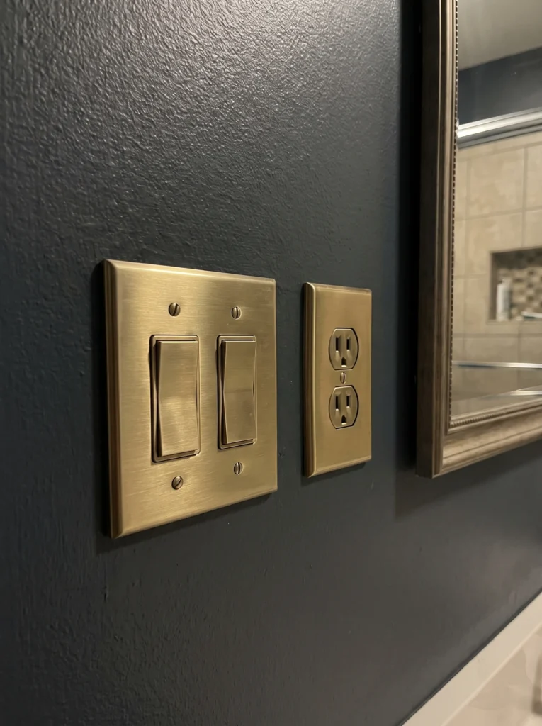 brushed brass outlet cover and light switch plate on a dark painted bathroom wall