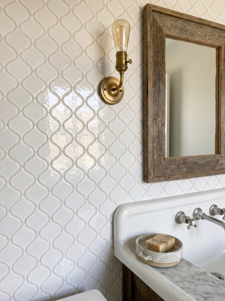 glossy white arabesque tile wall with a brass sconce