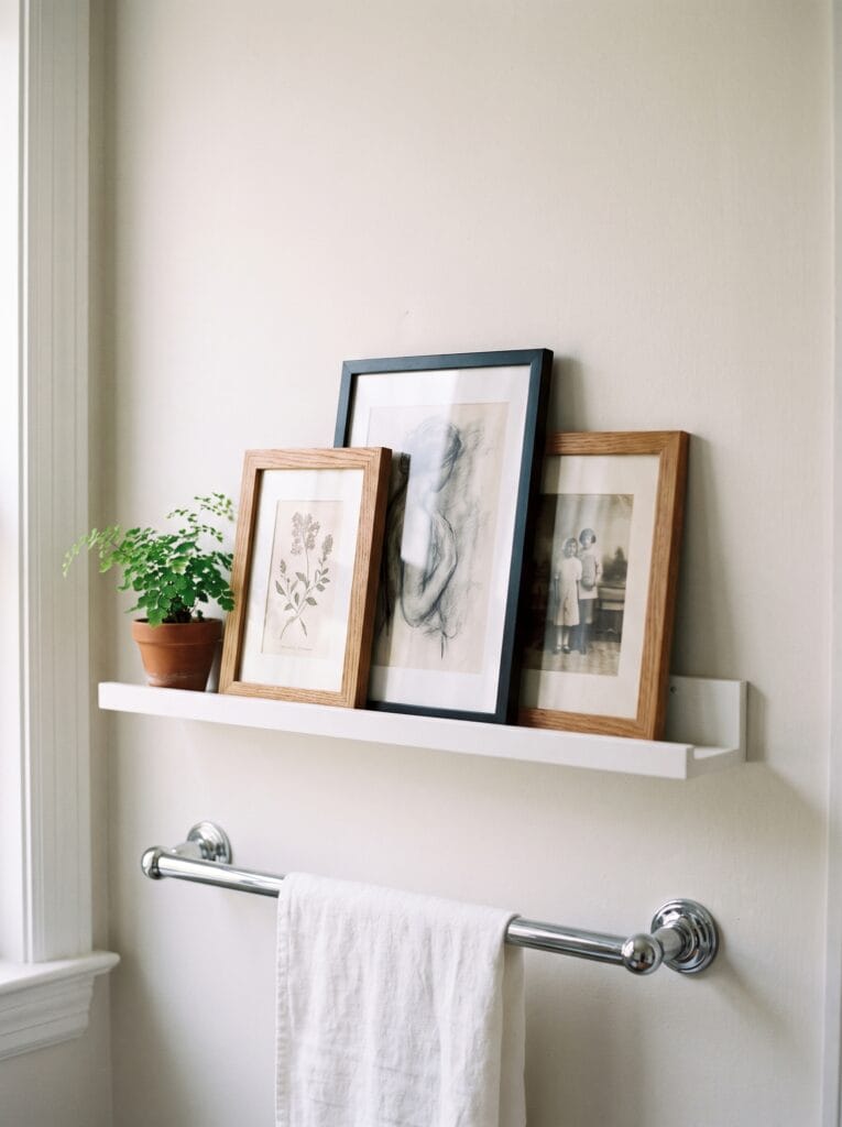 Three small framed prints overlapping on a white picture ledge above a chrome towel bar