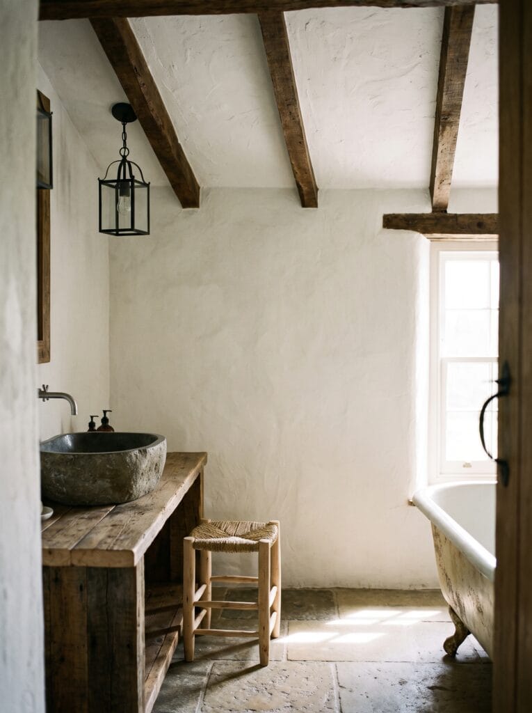 A rustic white plaster bathroom ceiling with exposed dark timber beams and a black lantern pendant