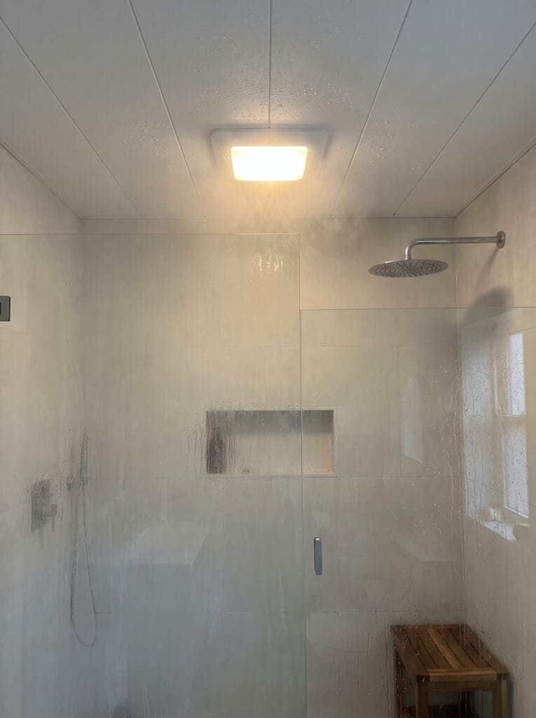 A steamy shower with waterproof white ceiling panels and a flush IP-rated light fitting