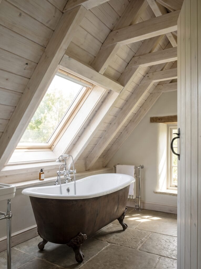 A vaulted bathroom ceiling clad in pale limed timber with exposed trusses and a skylight