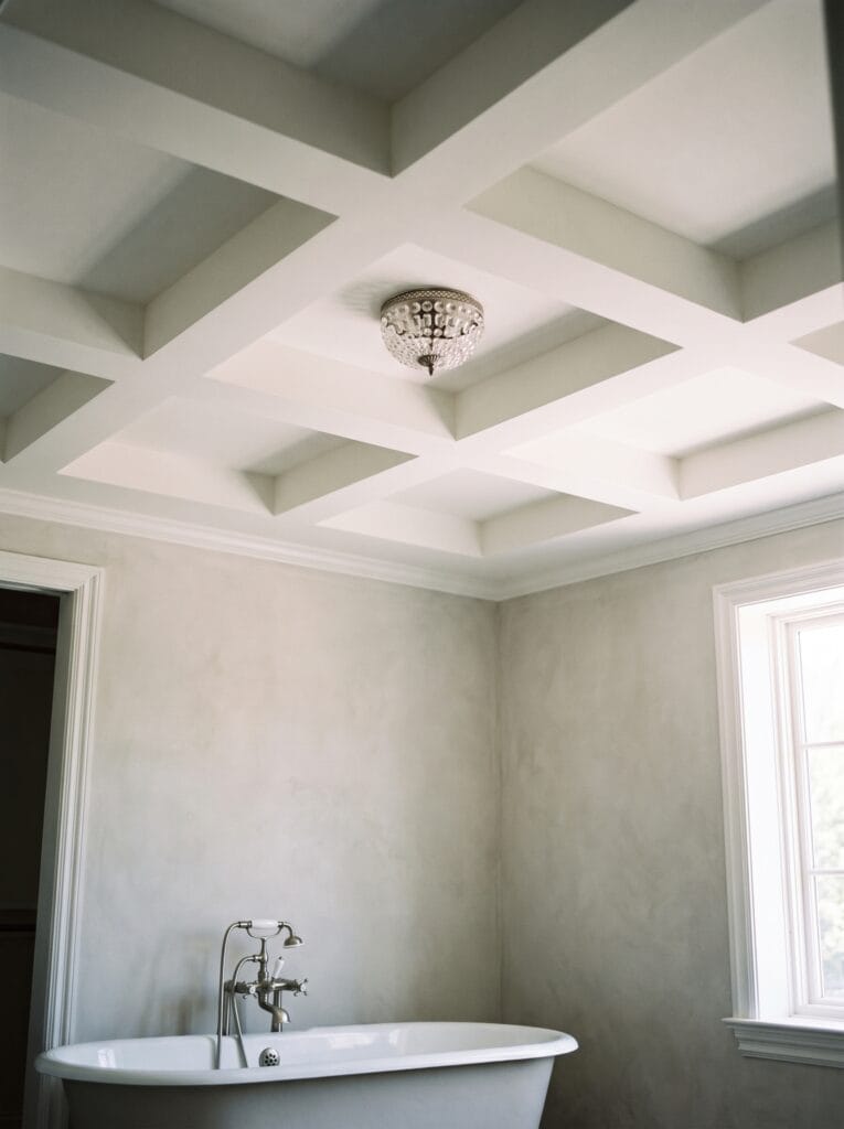 A white coffered bathroom ceiling with deep recessed panels and a crystal flush mount