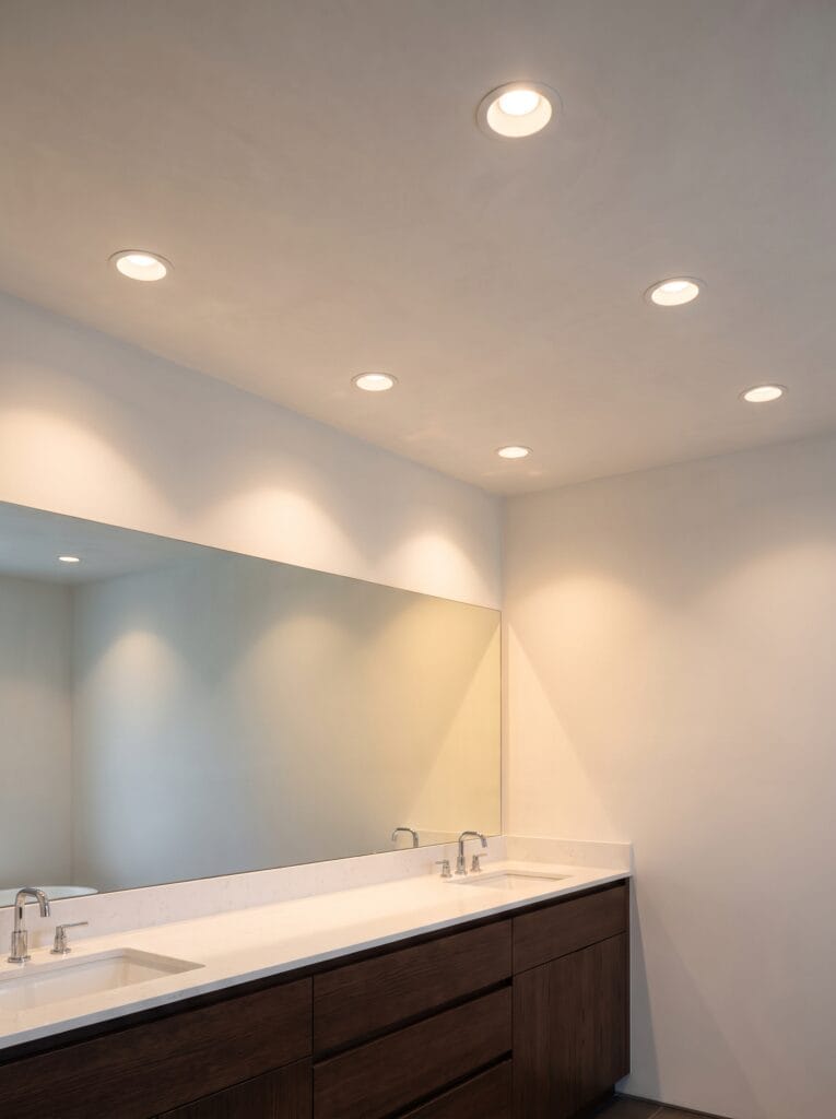 A flat white plaster bathroom ceiling with recessed downlights spaced above a long vanity and wide mirror