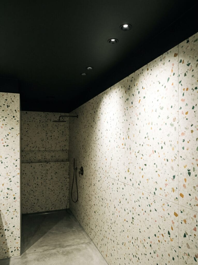 A dark painted bathroom ceiling with black-trimmed recessed spotlights above terrazzo walls