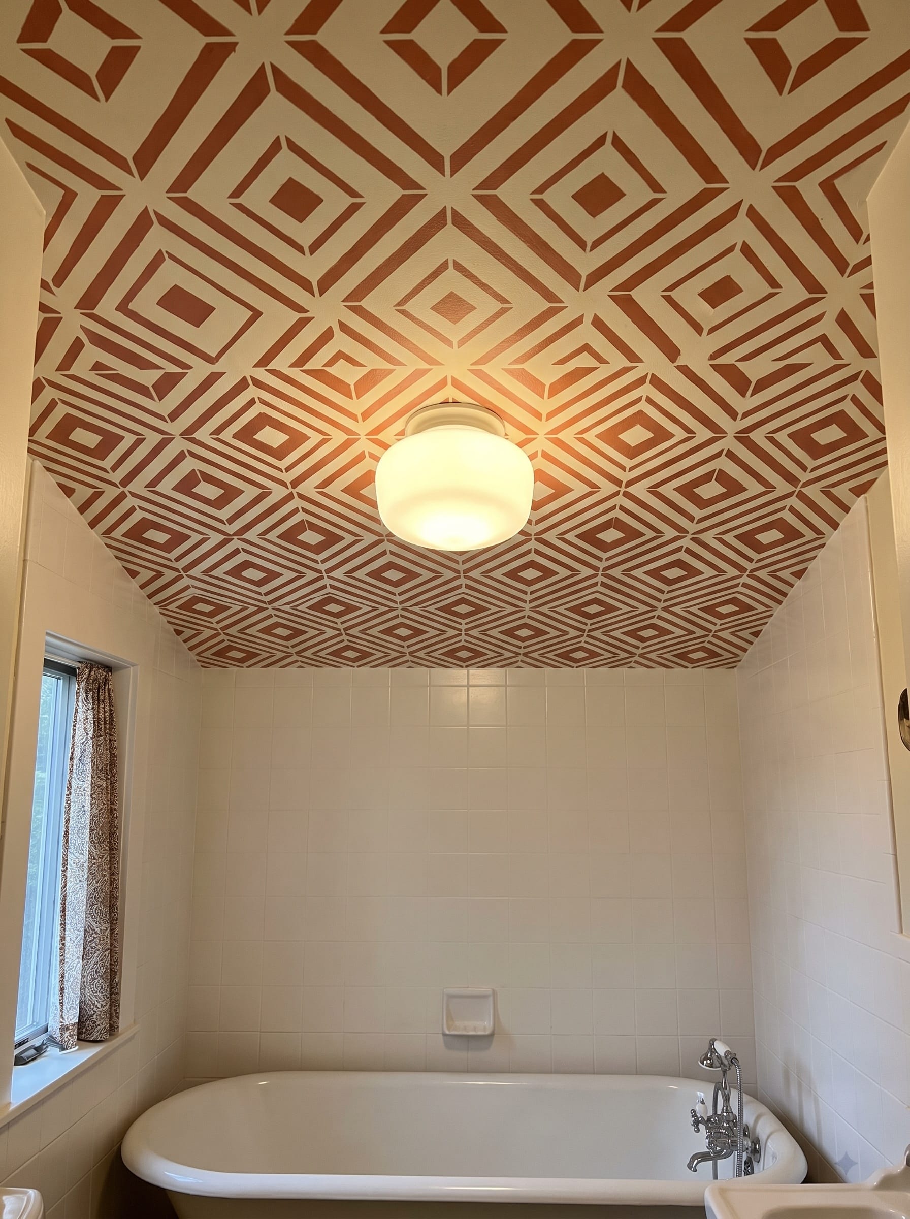 A bold terracotta geometric pattern stencilled across a small bathroom ceiling above a tub alcove