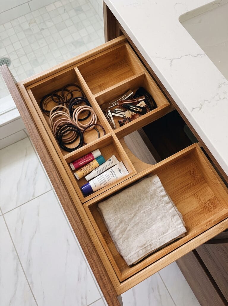 A vanity drawer fitted with bamboo dividers separating hair ties, clips, balms and a folded cloth