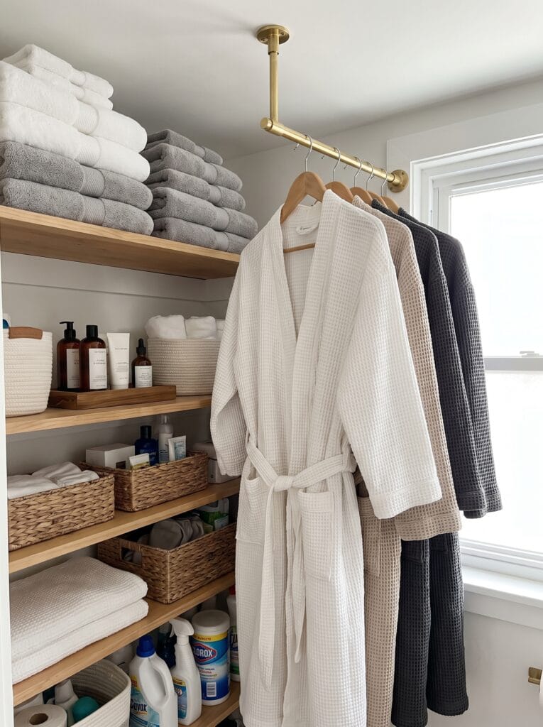 A brass rail mounted in a linen closet holding waffle robes on wooden hangers