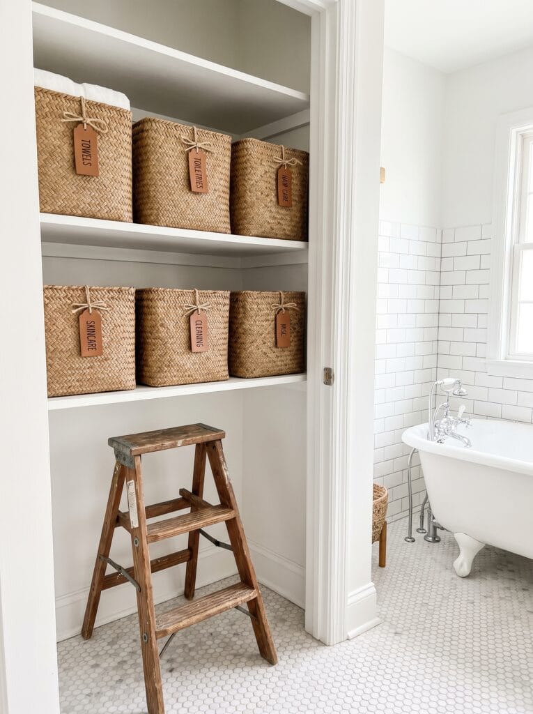 A closet shelf lined with matching woven seagrass baskets, each with a leather label tag