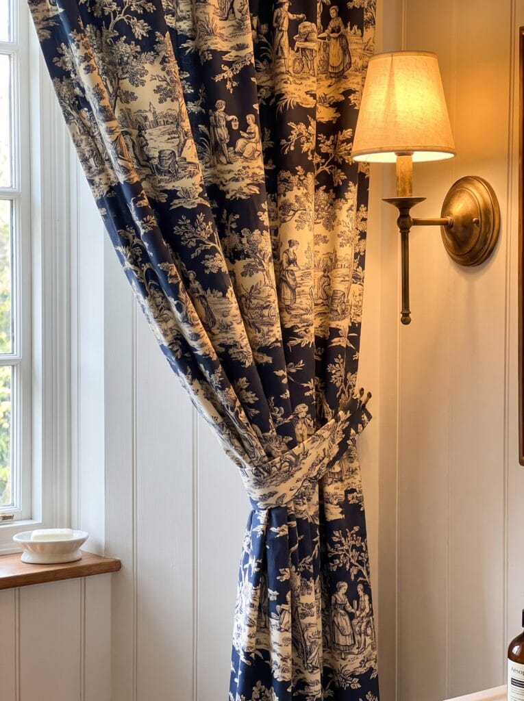 Navy and cream toile curtain tied back beside a brass wall sconce