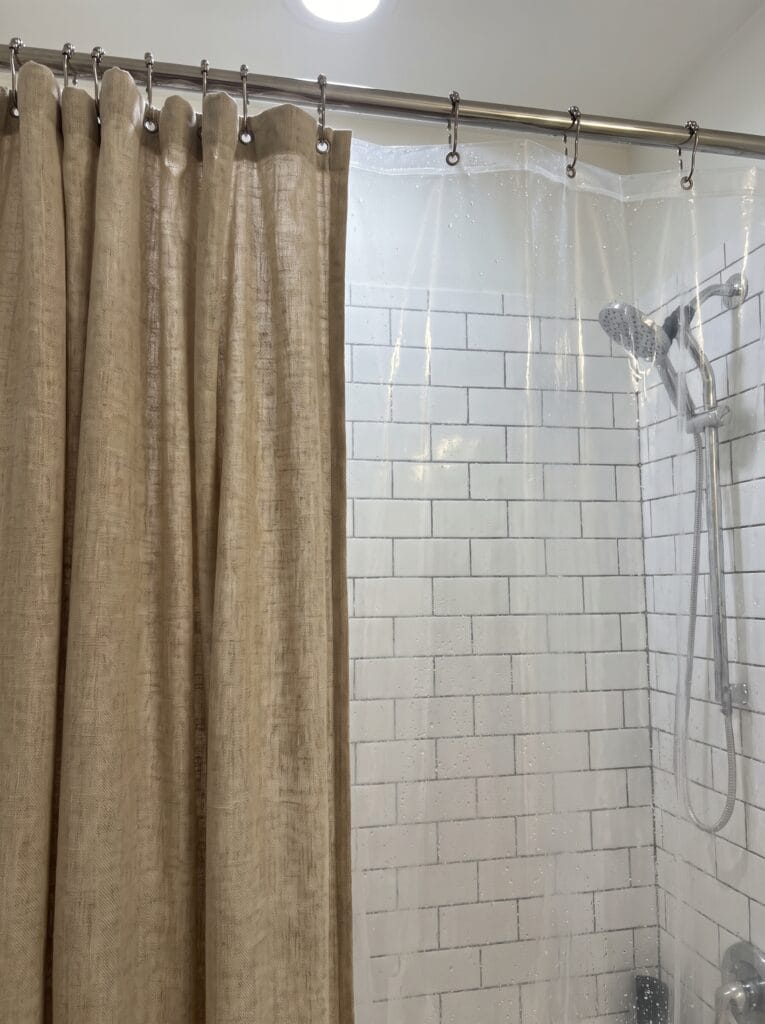 Linen outer shower curtain pulled open to show a clear waterproof liner behind it