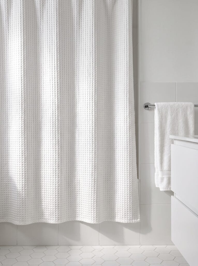 White waffle weave shower curtain in an all-white bathroom with hex floor tile