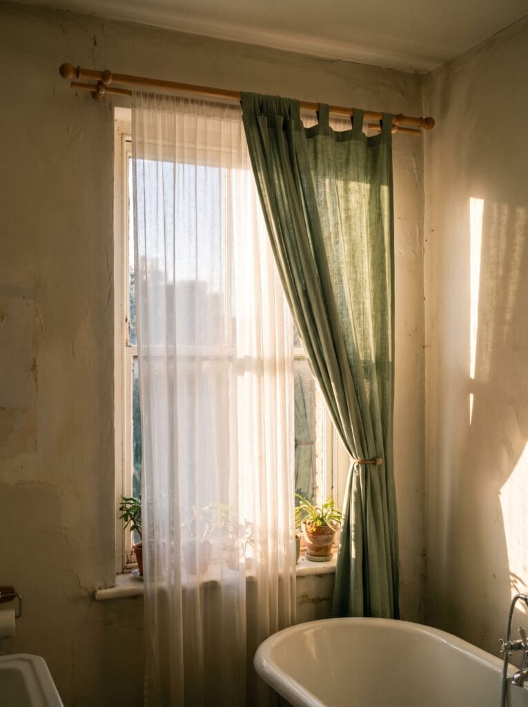 Layered white sheer and sage green curtain panels at a bathroom window