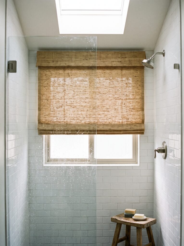 Woven natural shade over a small window inside a tiled shower enclosure