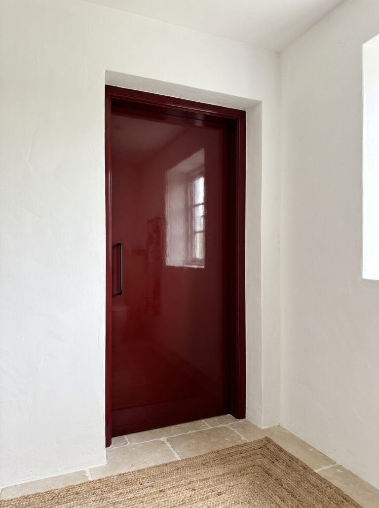 Deep glossy oxblood red bathroom door against chalk white plaster walls