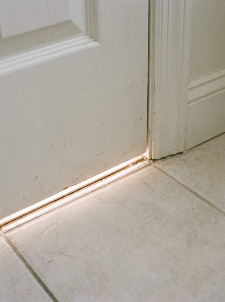 Close view of the bottom edge of a bathroom door with light spilling through the gap
