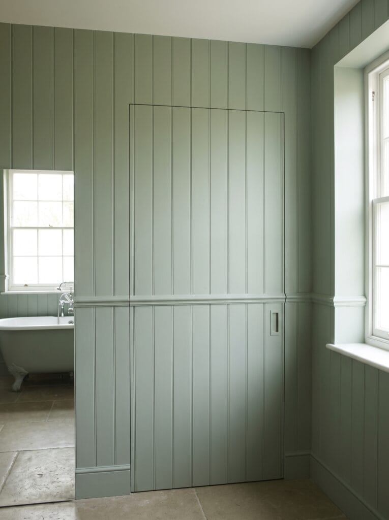 Bathroom door built flush into painted wall panelling with no visible frame
