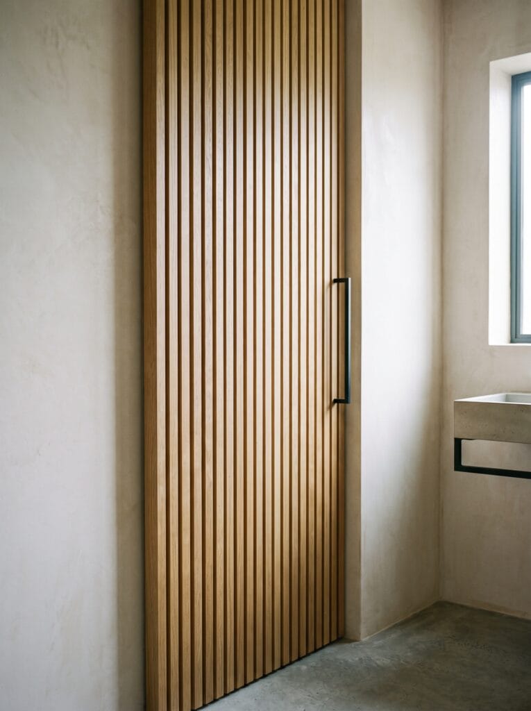 Bathroom door faced with narrow vertical oak battens and a slim black pull