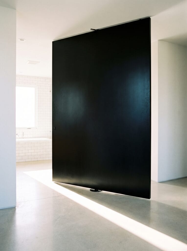 Tall matte black pivot door standing half open on a central floor pivot