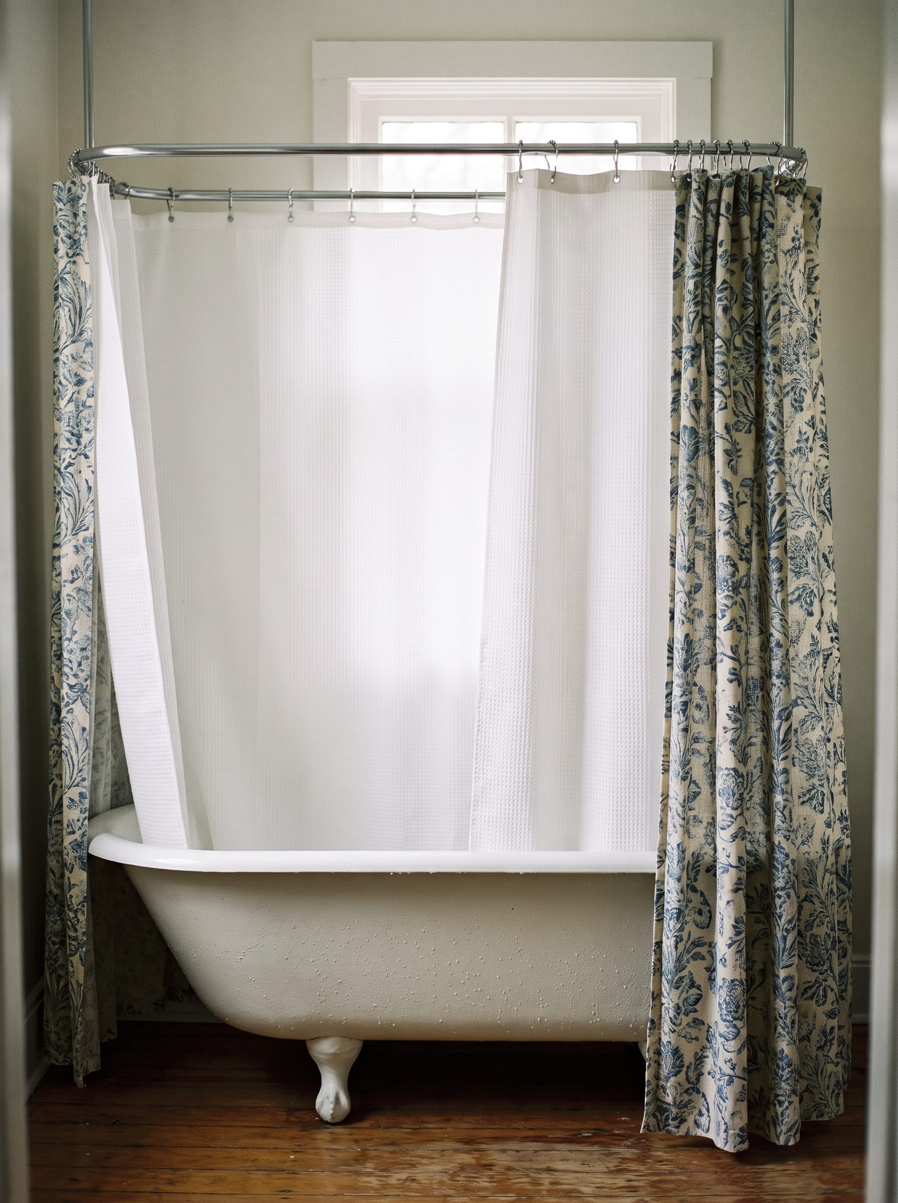 White waffle shower liner hanging inside a patterned linen outer curtain on a chrome rod