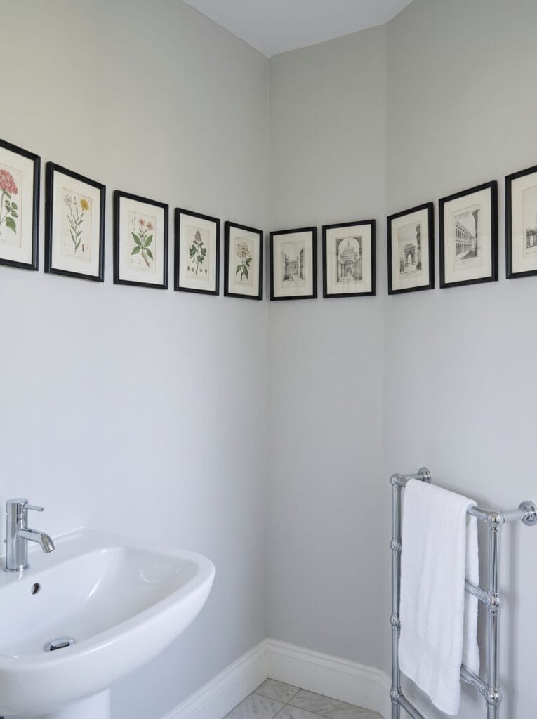 Continuous row of black framed prints running around a bathroom corner at picture rail height