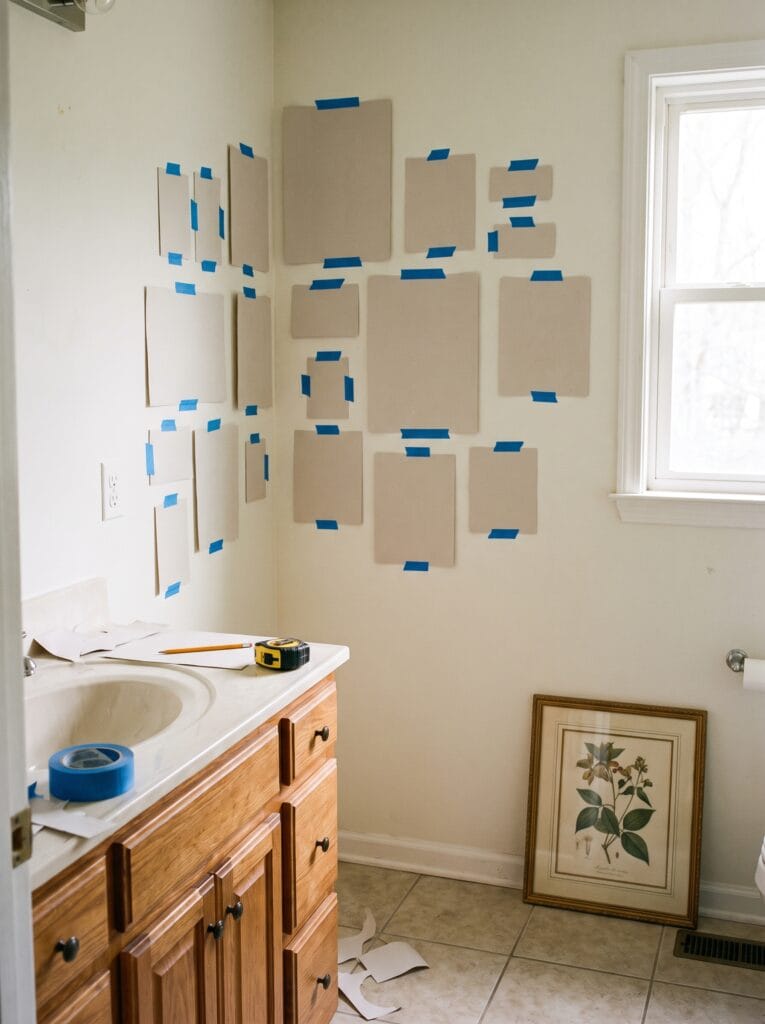 Paper templates taped to a bathroom wall with a tape measure and pencil on the vanity