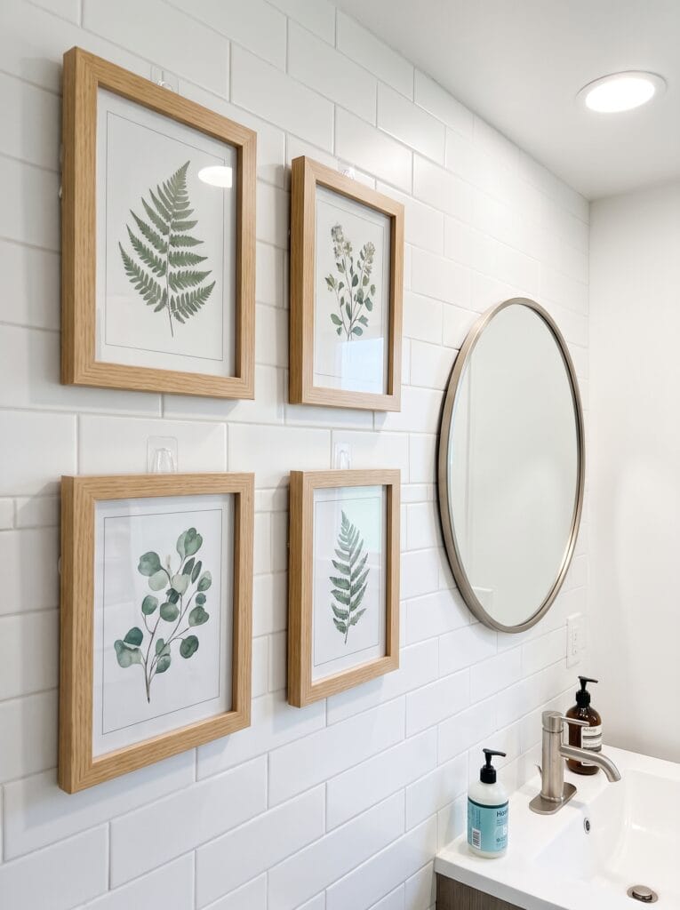 Four oak framed botanical prints on white subway tile mounted with clear adhesive hooks