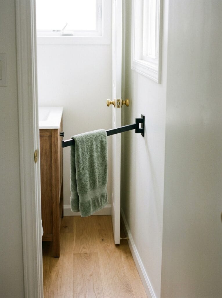 Matte black swing-arm towel bar beside a bathroom doorway holding a sage green hand towel