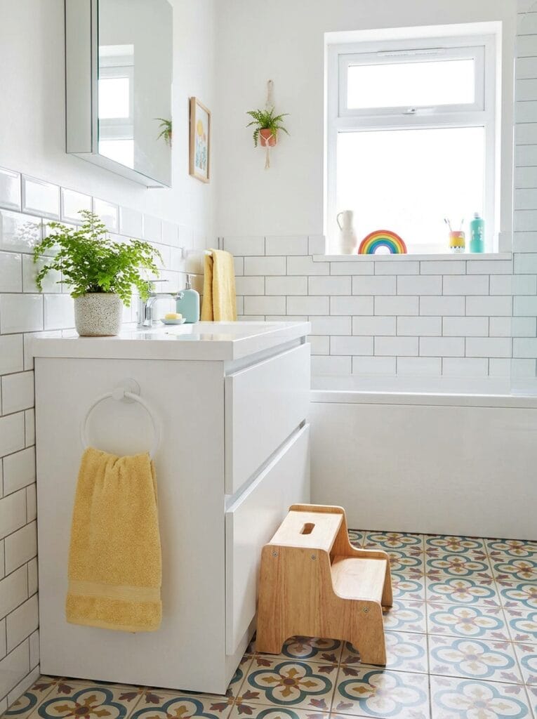 White towel ring mounted low on the side of a white vanity with a yellow hand towel and a wooden step stool