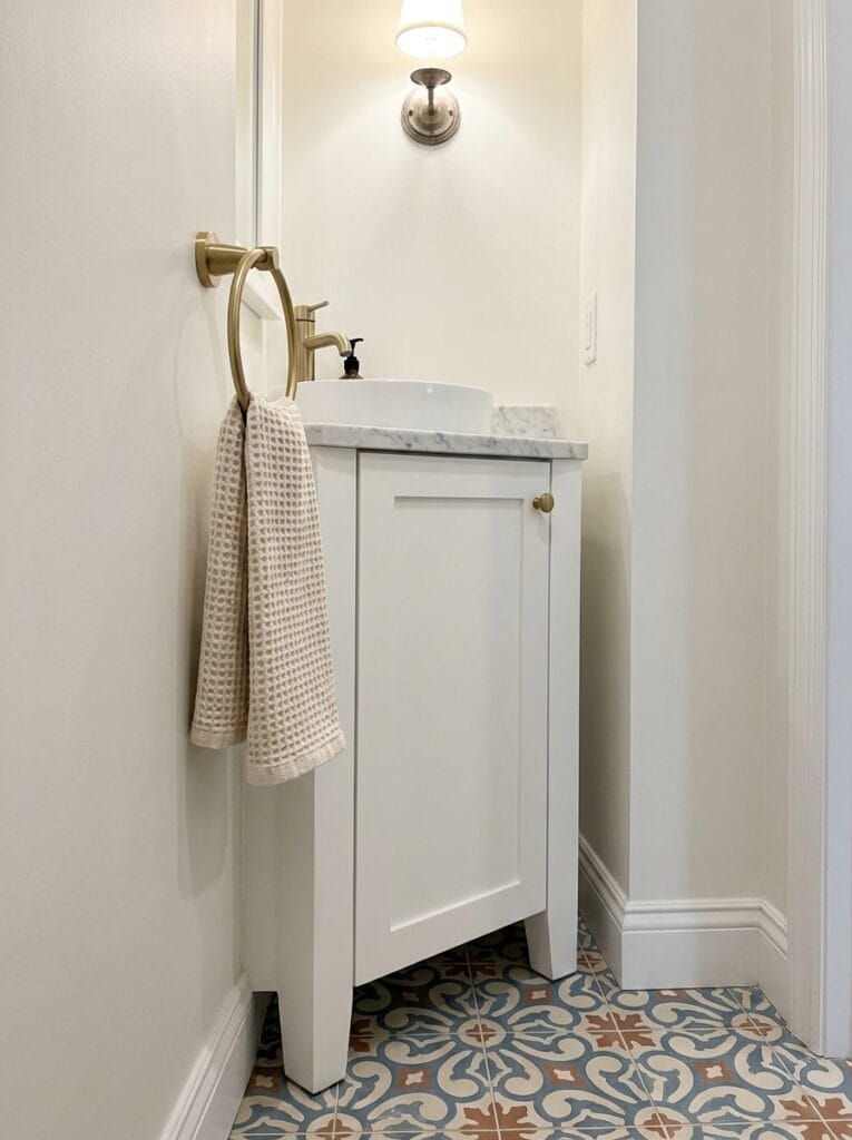 Brass towel ring on the side wall of an alcove next to a narrow white vanity with a textured hand towel