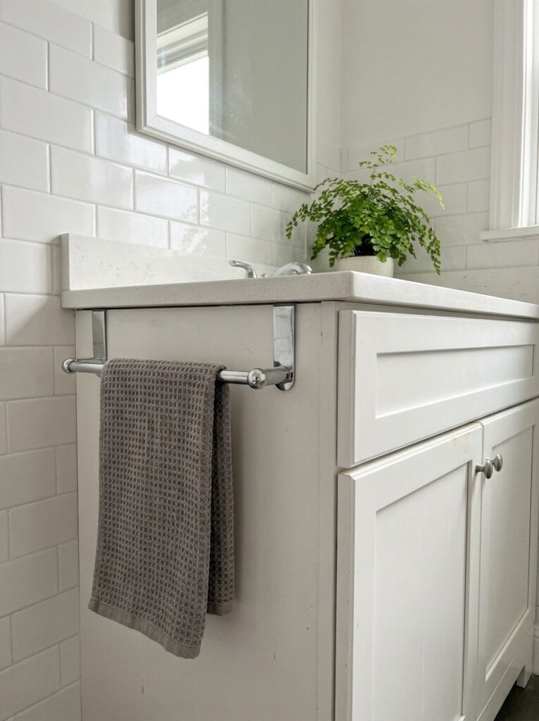 Chrome over-the-door towel bar on a white vanity cabinet holding a grey waffle hand towel
