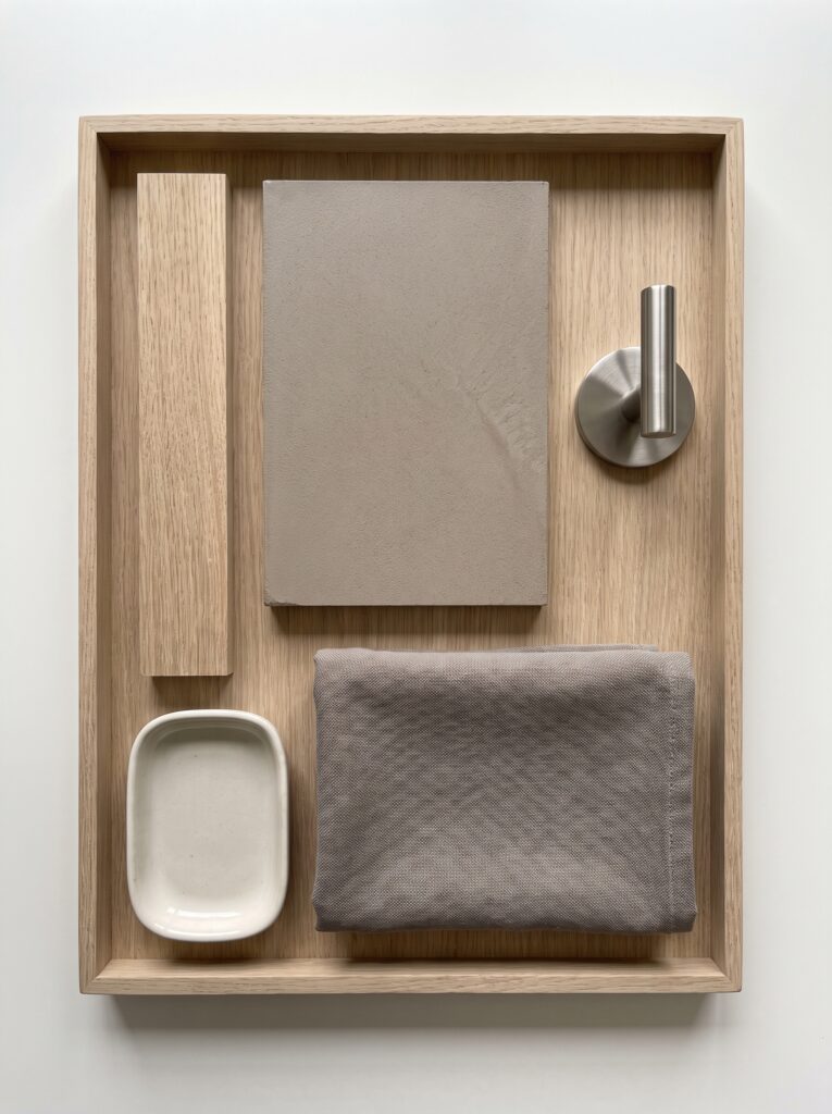 taupe microcement sample with white oak, a brushed stainless hook and a warm gray towel on an oak tray