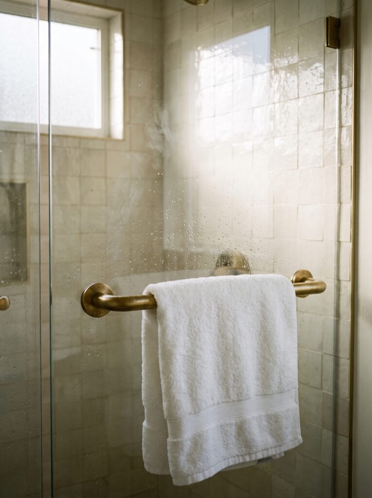 brushed brass towel bar mounted on a glass shower panel with a folded white towel