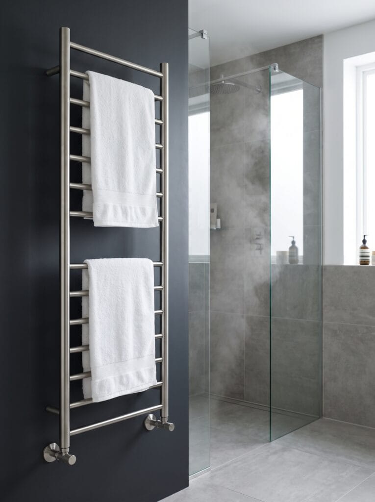brushed steel heated towel rail on a charcoal wall beside a walk-in glass shower