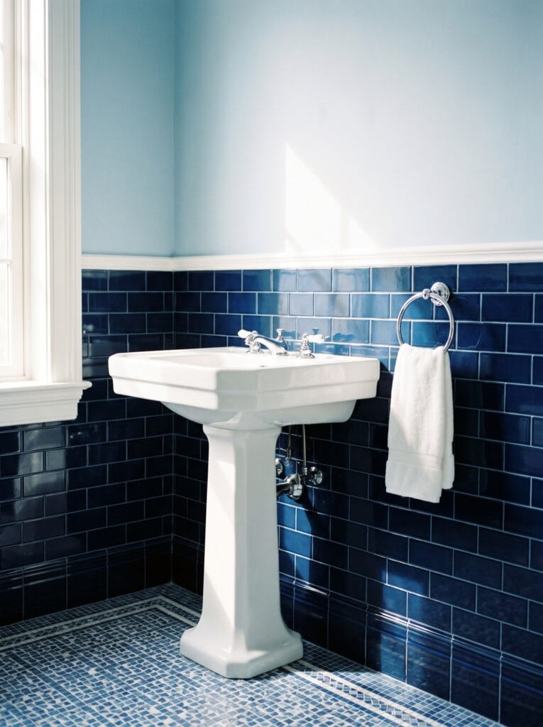 A bathroom with glossy navy subway tile to chair height, pale blue walls above and a blue mosaic tile floor