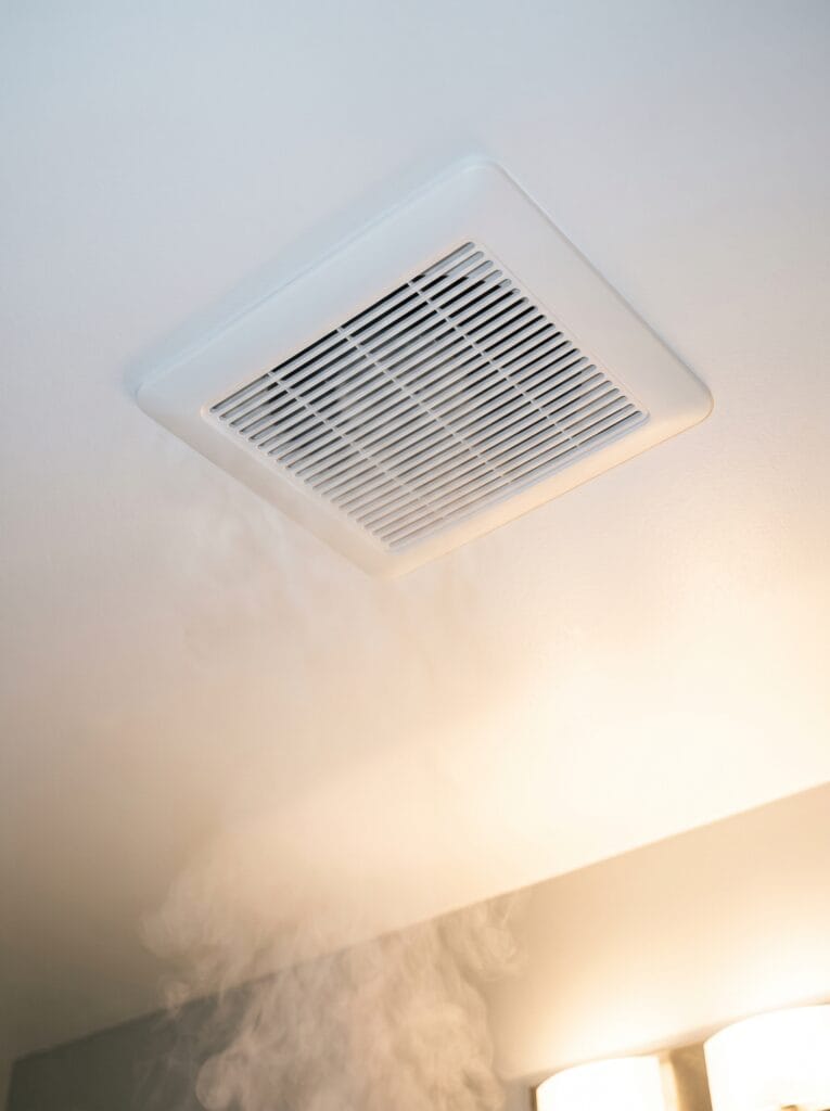 Bathroom exhaust fan grille in a white ceiling with steam drifting up toward it