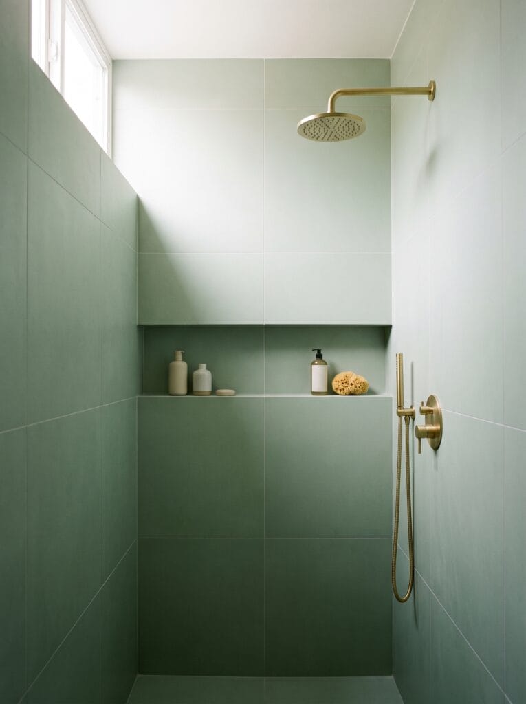 Large-format soft green porcelain tile in a compact shower with a niche