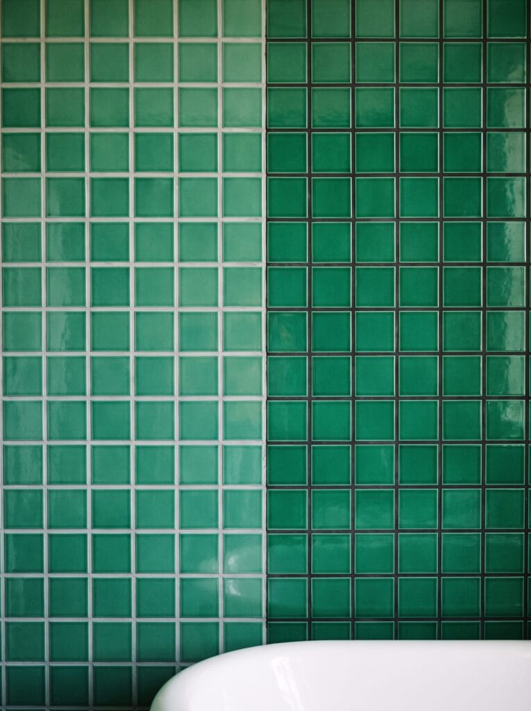 Emerald green square tile with pale grey grout on the left and charcoal grout on the right