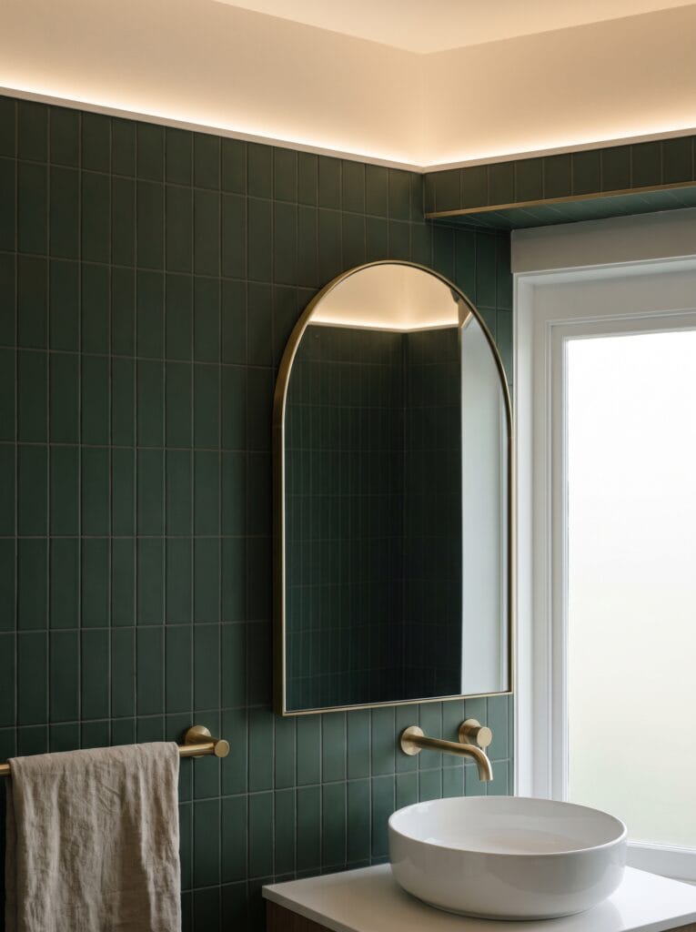 Forest green bathroom tile wall with an arched brass mirror and vessel basin